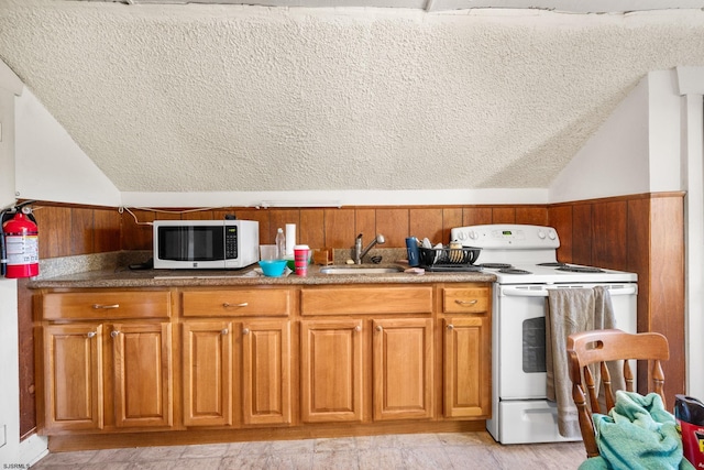 kitchen featuring a textured ceiling, wood walls, white appliances, and sink