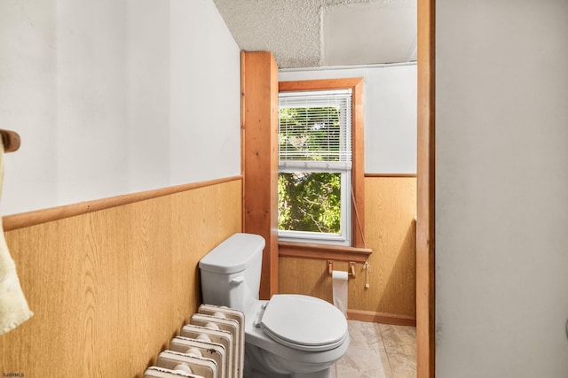 bathroom with wooden walls, radiator heating unit, tile patterned flooring, and toilet