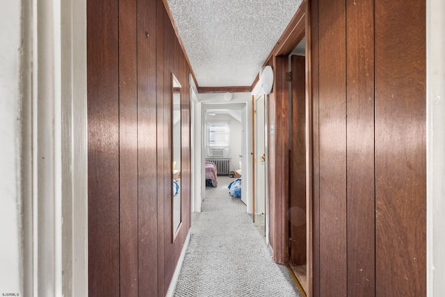 hall with wood walls, radiator heating unit, light colored carpet, and a textured ceiling