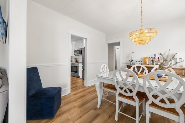 dining room with an inviting chandelier, ornamental molding, and light hardwood / wood-style flooring