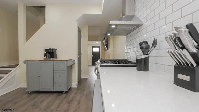 kitchen with gray cabinetry, wall chimney exhaust hood, dark wood-type flooring, decorative backsplash, and stainless steel stove