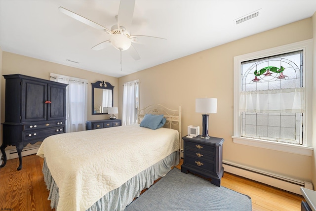 bedroom featuring hardwood / wood-style flooring, ceiling fan, a baseboard heating unit, and multiple windows