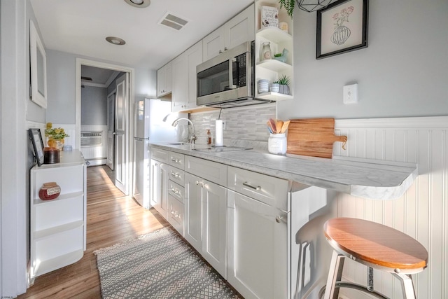 kitchen with appliances with stainless steel finishes, light wood-type flooring, a kitchen breakfast bar, sink, and white cabinets