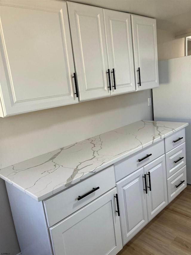 kitchen with white cabinetry, light hardwood / wood-style flooring, and light stone countertops