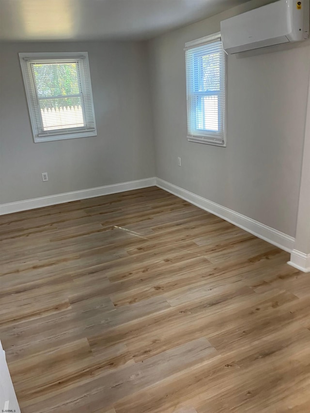 unfurnished room with light wood-type flooring, an AC wall unit, and plenty of natural light