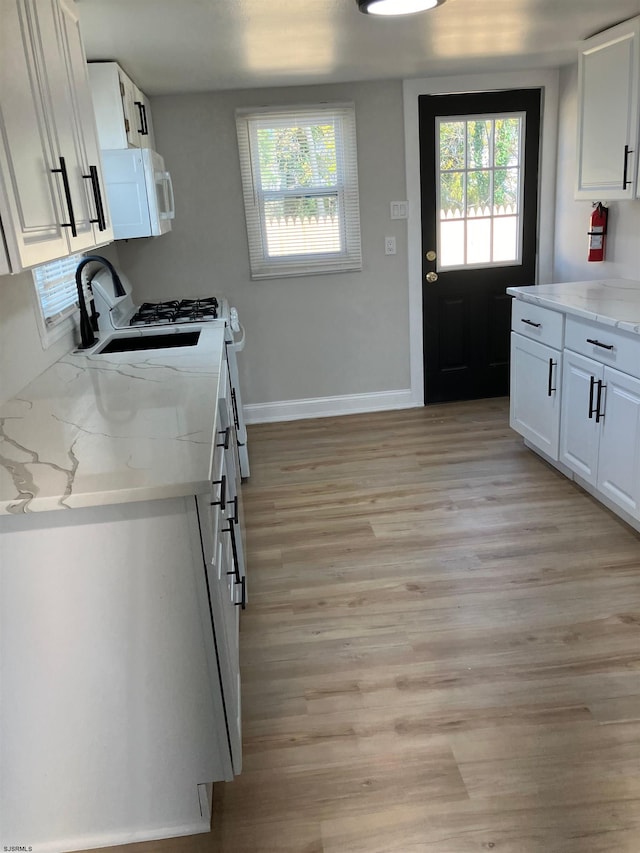 kitchen with light stone countertops, light hardwood / wood-style flooring, and white cabinetry