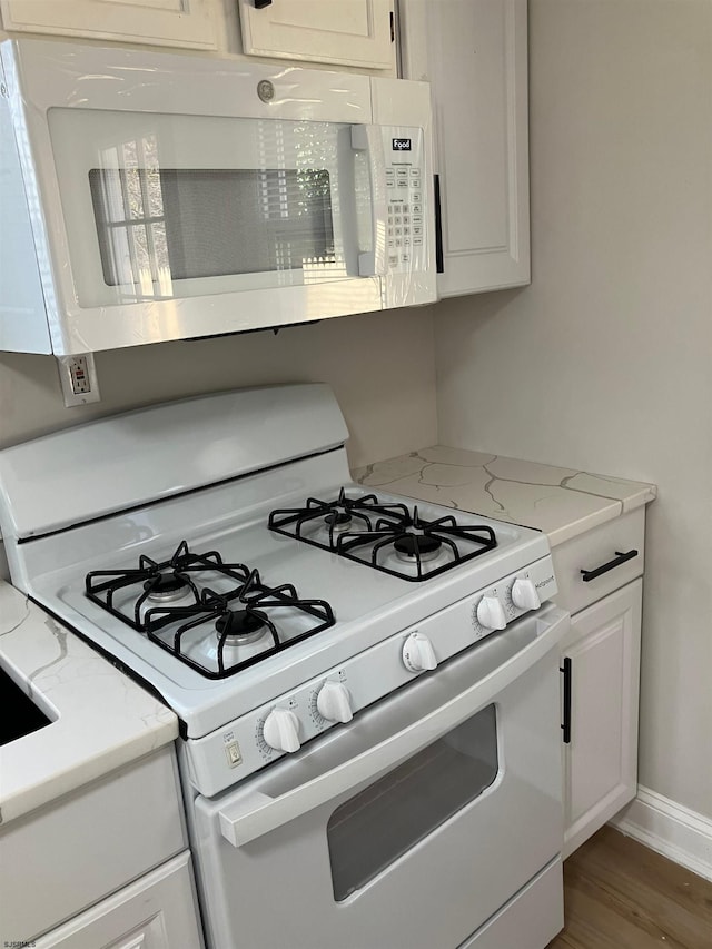 kitchen with light stone countertops, white cabinets, white appliances, and hardwood / wood-style flooring