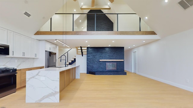 kitchen with white cabinets, hanging light fixtures, a large island, range, and light stone counters