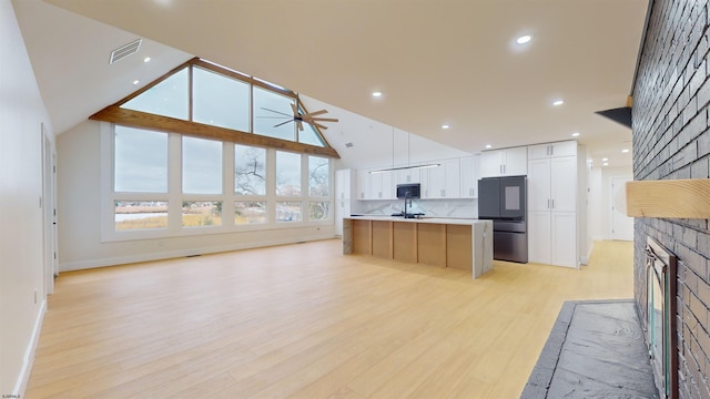 kitchen with a large island, stainless steel fridge, white cabinets, a brick fireplace, and light wood-type flooring