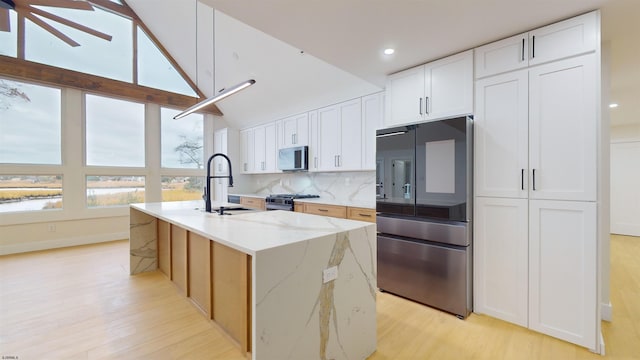 kitchen featuring appliances with stainless steel finishes, sink, white cabinets, a kitchen island with sink, and light stone counters