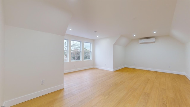 additional living space featuring vaulted ceiling, an AC wall unit, and light hardwood / wood-style flooring