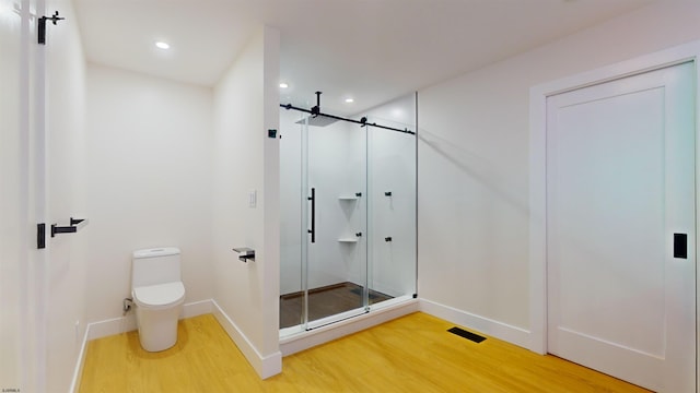 bathroom featuring hardwood / wood-style floors, a shower with shower door, and toilet