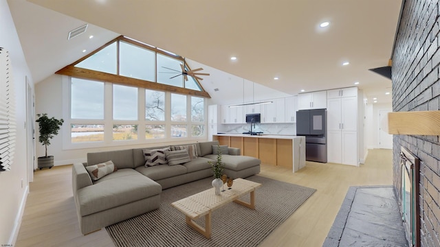 living room featuring a fireplace, high vaulted ceiling, ceiling fan, and light wood-type flooring