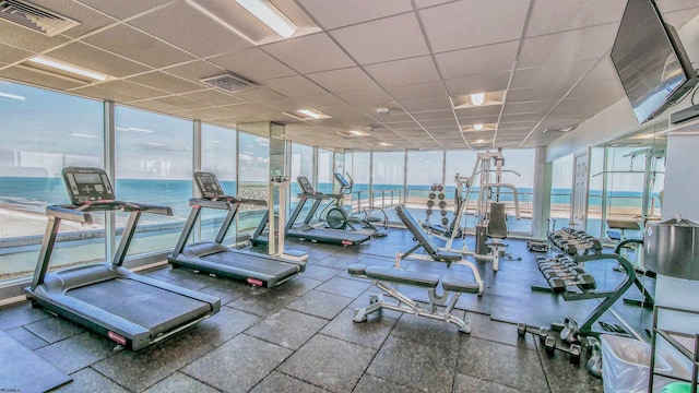 exercise room featuring a paneled ceiling, floor to ceiling windows, and a water view