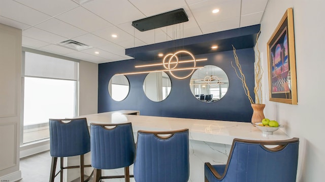 bar with a paneled ceiling and light stone countertops