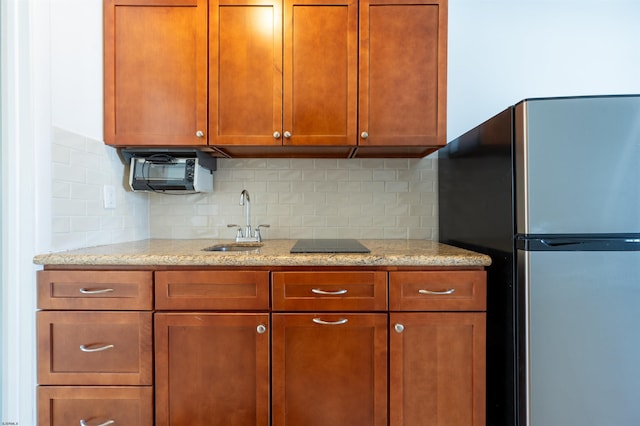 kitchen featuring stainless steel fridge, sink, light stone countertops, and backsplash