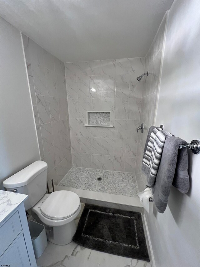 bathroom featuring a tile shower, vanity, and toilet