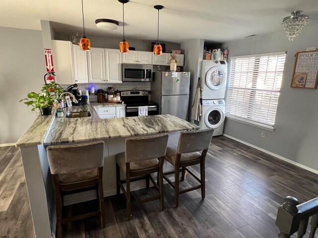 kitchen featuring pendant lighting, sink, appliances with stainless steel finishes, stacked washer / drying machine, and kitchen peninsula