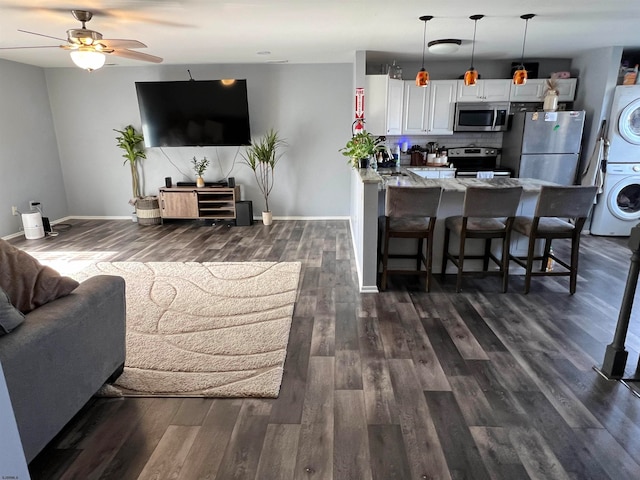 living room featuring stacked washer / drying machine, sink, dark hardwood / wood-style floors, and ceiling fan