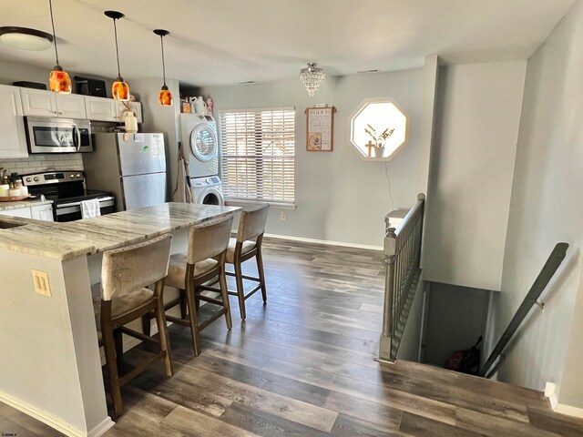 kitchen featuring pendant lighting, white cabinetry, stainless steel appliances, stacked washer / dryer, and a kitchen bar