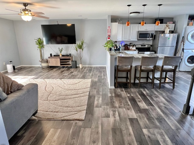 living room with ceiling fan, stacked washer and clothes dryer, dark hardwood / wood-style floors, and sink