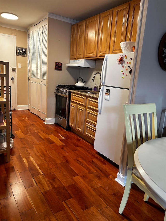 kitchen featuring crown molding, dark stone countertops, stainless steel gas stove, white fridge, and dark hardwood / wood-style floors