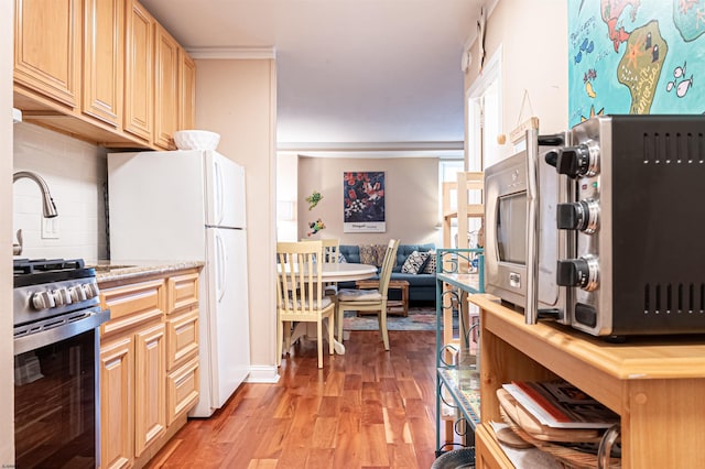 kitchen with light hardwood / wood-style flooring, stainless steel gas stove, ornamental molding, tasteful backsplash, and white fridge