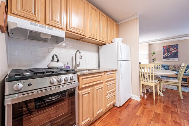 kitchen with sink, white refrigerator, backsplash, stainless steel stove, and light wood-type flooring