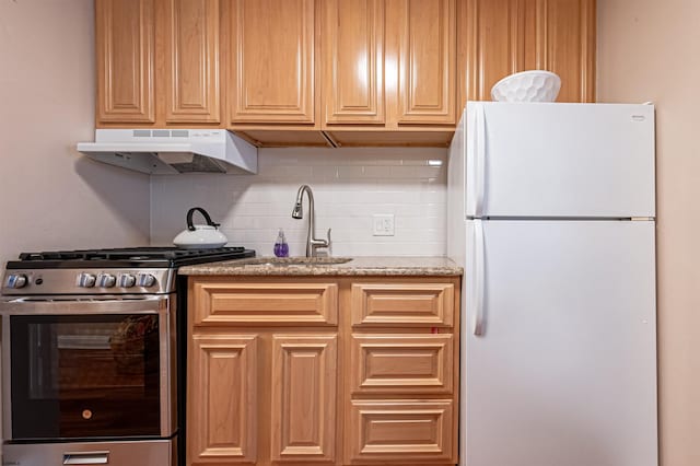 kitchen featuring light stone countertops, sink, backsplash, white fridge, and high end stainless steel range