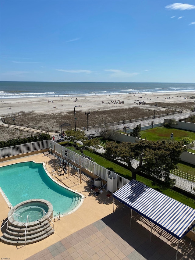 view of swimming pool with a water view, an in ground hot tub, a patio, and a view of the beach