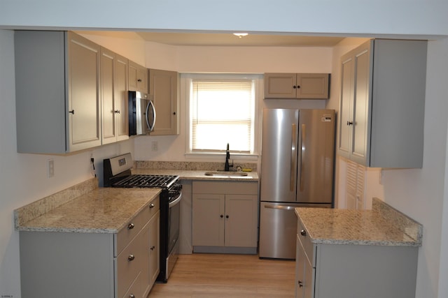 kitchen with appliances with stainless steel finishes, light stone counters, gray cabinetry, sink, and light hardwood / wood-style flooring