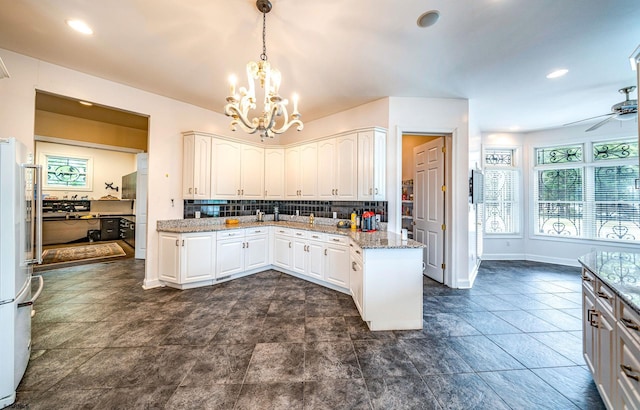 kitchen with light stone countertops, backsplash, white refrigerator, decorative light fixtures, and white cabinets