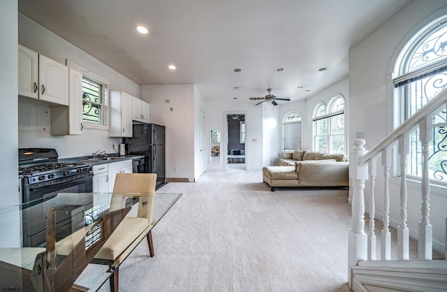 kitchen featuring black appliances, a healthy amount of sunlight, white cabinets, and light colored carpet