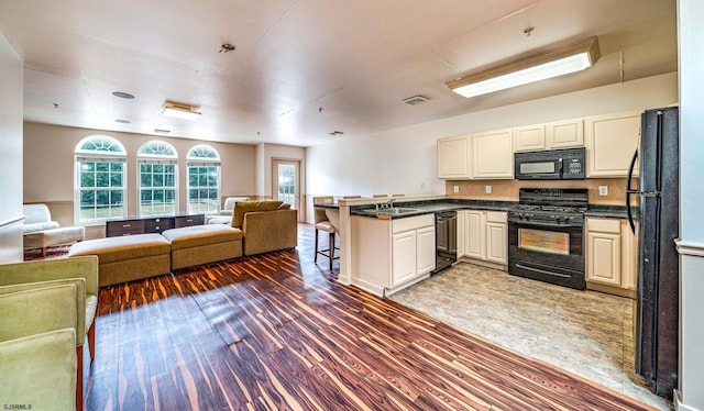 kitchen with kitchen peninsula, dark hardwood / wood-style flooring, a breakfast bar, sink, and black appliances