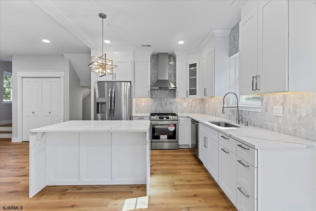 kitchen with white cabinets, wall chimney range hood, sink, appliances with stainless steel finishes, and a kitchen island