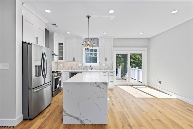 kitchen featuring white cabinets, appliances with stainless steel finishes, light wood-type flooring, and pendant lighting