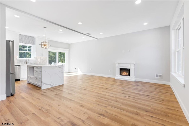 unfurnished living room with light wood-type flooring, a notable chandelier, and sink