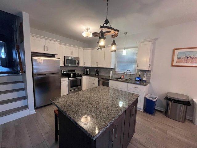 kitchen with white cabinets, decorative light fixtures, a kitchen island, and appliances with stainless steel finishes