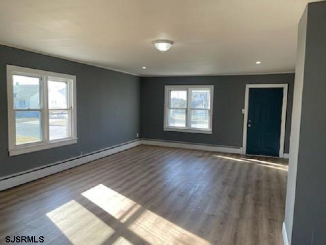 empty room featuring dark hardwood / wood-style floors, a healthy amount of sunlight, and a baseboard heating unit