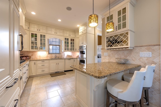 kitchen featuring sink, stainless steel double oven, light stone counters, decorative light fixtures, and a breakfast bar area