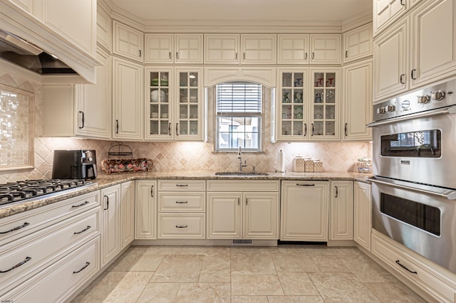 kitchen featuring custom exhaust hood, backsplash, sink, appliances with stainless steel finishes, and light stone counters