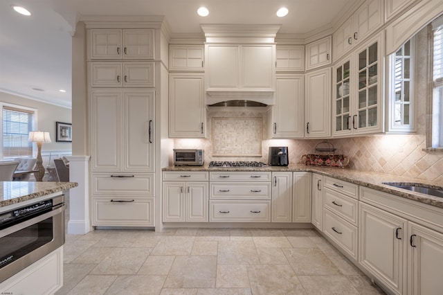 kitchen featuring decorative backsplash, light stone counters, ornamental molding, custom exhaust hood, and stainless steel appliances