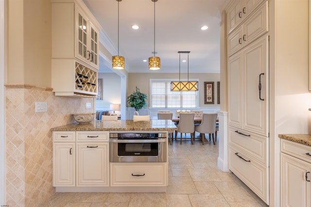 kitchen with crown molding, stainless steel oven, light stone counters, and hanging light fixtures