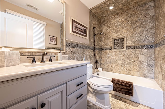 full bathroom featuring tiled shower / bath combo, toilet, tile walls, and vanity