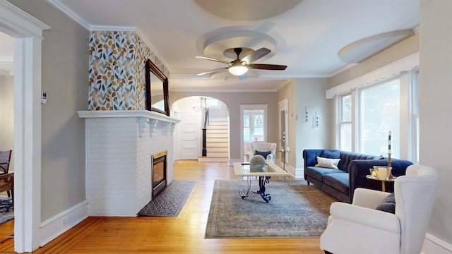 living room featuring a fireplace, light hardwood / wood-style flooring, ceiling fan, and crown molding