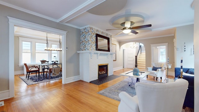 living room featuring hardwood / wood-style flooring, ceiling fan, crown molding, and a brick fireplace