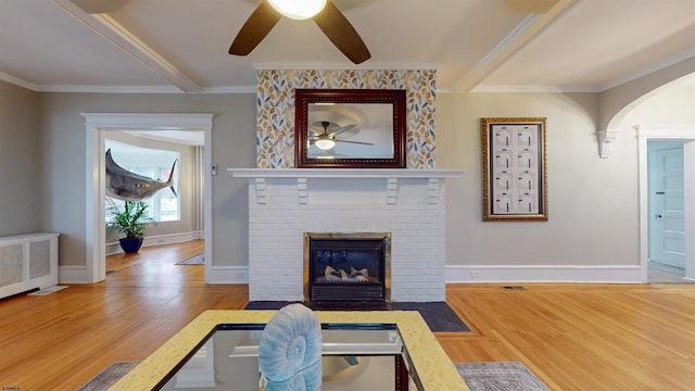 living room featuring ceiling fan, crown molding, wood-type flooring, and a fireplace