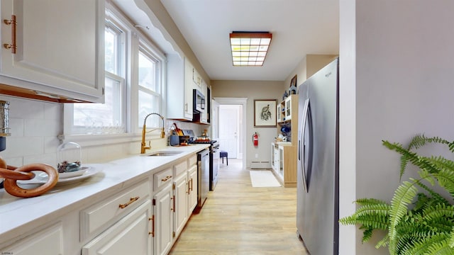 kitchen with decorative backsplash, appliances with stainless steel finishes, sink, light hardwood / wood-style floors, and white cabinetry