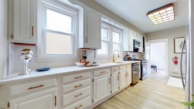 kitchen featuring backsplash, sink, light wood-type flooring, white cabinetry, and stainless steel appliances