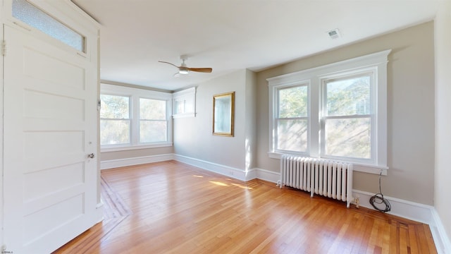 empty room featuring ceiling fan, a healthy amount of sunlight, radiator heating unit, and light hardwood / wood-style flooring